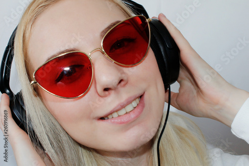 Close-up portrait of happy young woman with blonde hair listening music . Smiling Woman with in headphones listening to music on white background , top view. Attractive funny model. Copy Space.