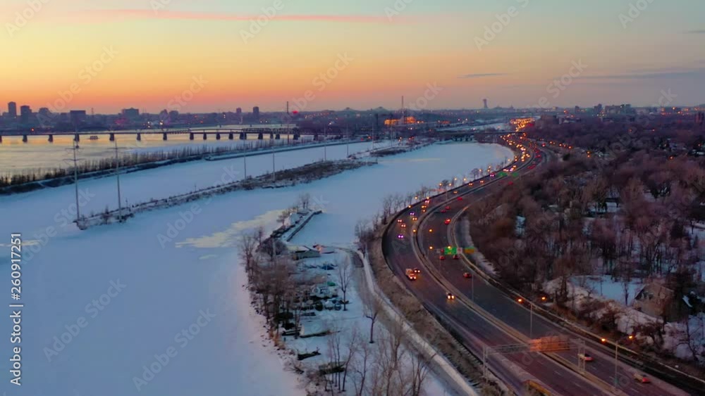A slow moving aerial shot at twilight that flies over a half-frozen river, showing a long bridge and a brightly city in the background A slow moving aerial shot at twilight that flies over a half-frozen river, showing a long bridge and a brightly city in the background