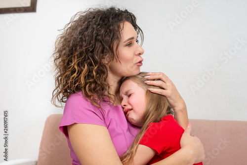 A young mother calms her little daughter. The girl is crying and her mother hugged her with love,