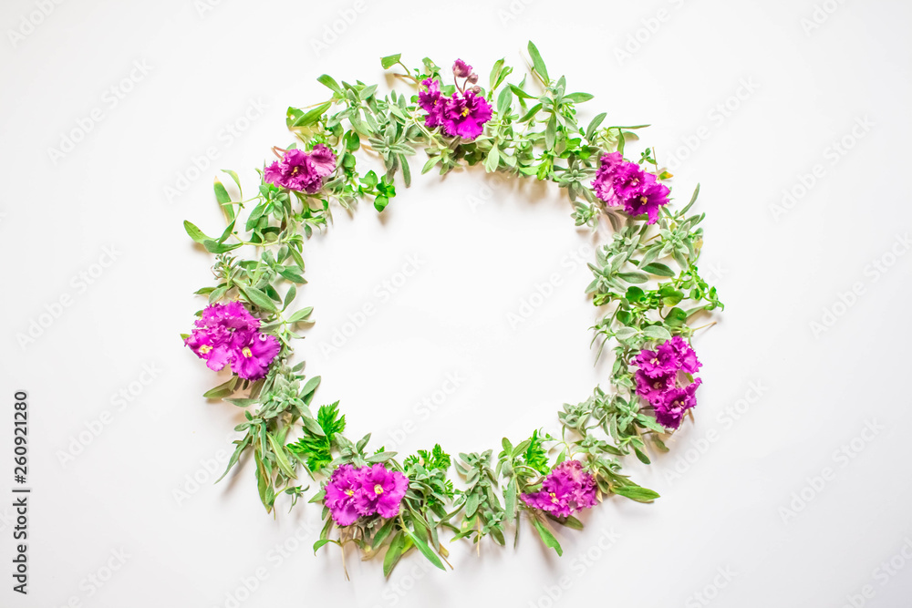 A wreath of violets on a white background. Round frame of purple flowers and fresh grass. Summer flowers. Flat lay, top view. A wreath of violets on a white background. Round frame of purple flowers and fresh grass. Summer flowers. Flat lay, top view.