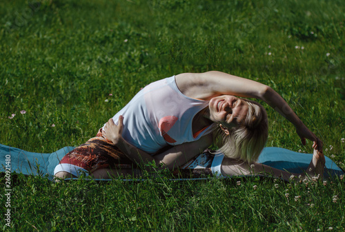 Blonde in a white t-shirt on the green grass doing yoga. Treatment and relaxation of the spine. Sports lifestyle © olga_polyanskaya