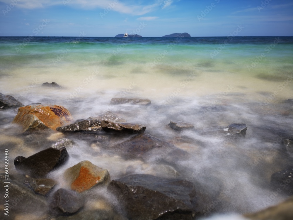 The beautiful silky smooth water waves and rocks on the sea shore during the sunny day.