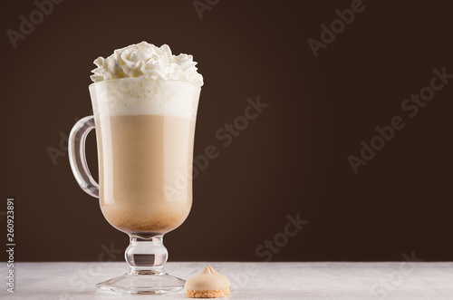 Hot coffee drink with whipped cream in wineglass with handle and cookies in dark brown interior on white wooden table, copy space.