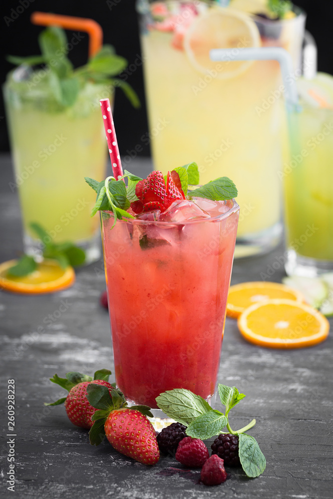 Cold strawberry drink on textured gray table. Lemonade pitcher and two glasses of fruit juice at the background out of focus. Cold strawberry drink on textured gray table. Lemonade pitcher and two glasses of fruit juice at the background out of focus.