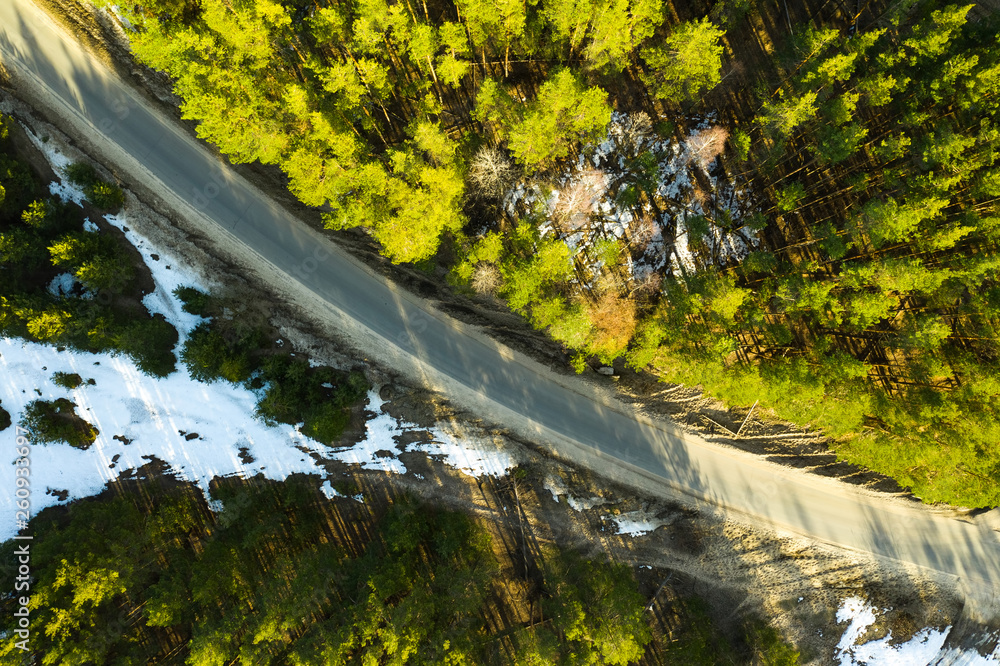 Old asphalt road in the spring forest top view Snow melts on the side of the road and between the trees. Old asphalt road in the spring forest top view Snow melts on the side of the road and between the trees.
