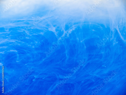 Blue acrylic ink in liquid, close up view. Abstract background. Paint dissolving into water. Abstract blue clouds swirling in water. Acrylic waves in liquid, abstract pattern. Blurred background