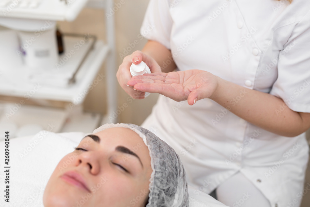 Hands of beautician apply cream to face of woman. Concept of beauty and youth. Close-up beautician causes moisturizer on the girl's face Hands of beautician apply cream to face of woman. Concept of beauty and youth. Close-up beautician causes moisturizer on the girl's face
