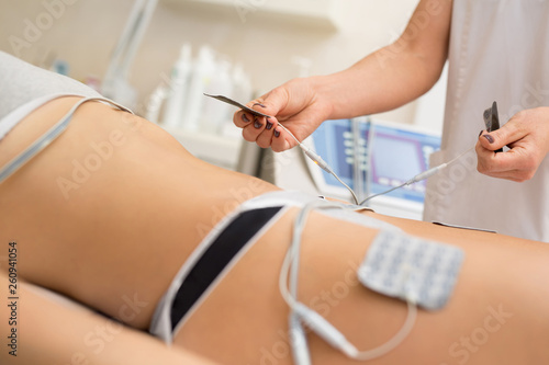 Therapist applying lipomassage on girls body in spa. Close-up of biostimulating apparatus for anti-cellulite lipomassage. Hardware cosmetology. Body care photo