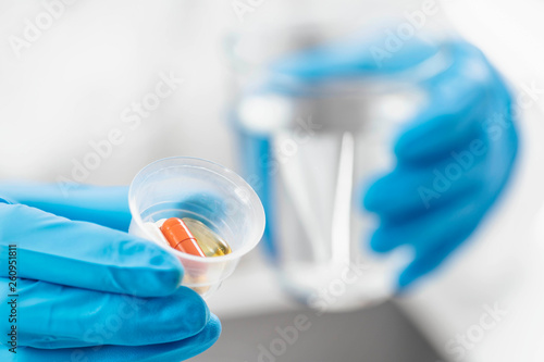Doctor`s Hand in a Glove Holding Graduated Medicine Cups with Pills