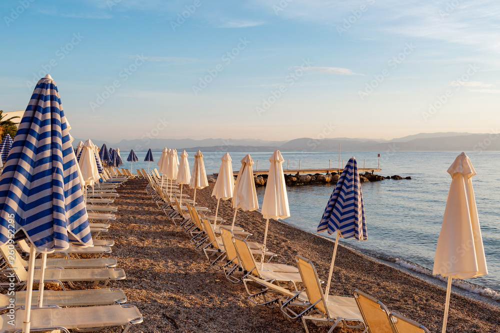 Summer sunrise on coast, Corfu island, Greece. Beach with Sunbeds and umbrellas with perfect views of the mainland Greece mountains.