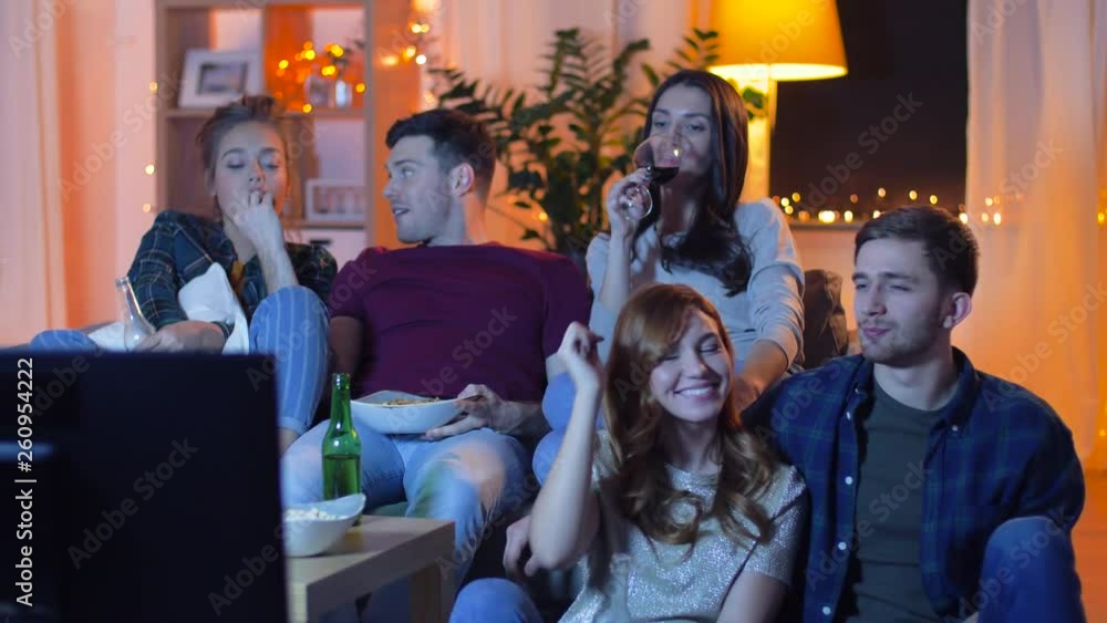 friendship and leisure concept - happy friends with non-alcoholic drinks and snacks watching tv at home in evening friendship and leisure concept - happy friends with non-alcoholic drinks and snacks watching tv at home in evening