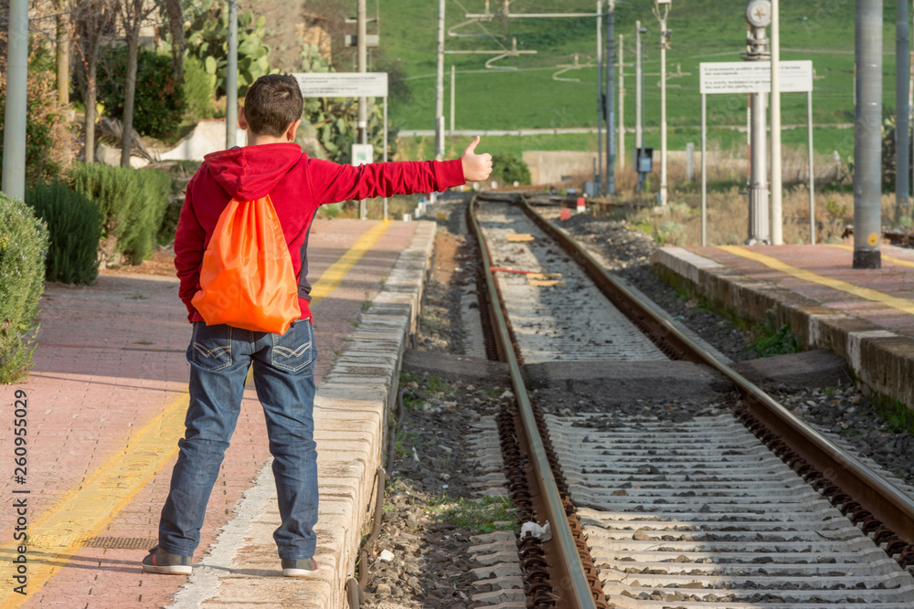 Young hitchhiker waiting of the train, standing on railway