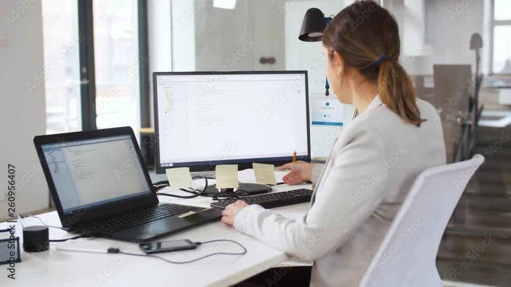 business, programming and technology concept - female programmer with notebook, sticky notes and computer working at office