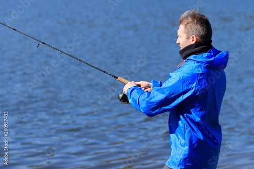 Fisherman with fishing rod on lake water background. A man catching fish by spinning on lakeside