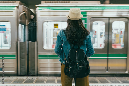 back view of young female backpacker stand on platform waiting subway train in underground station. Public transport people travel commute city urban concept. woman tourist watch metro drive leaving.