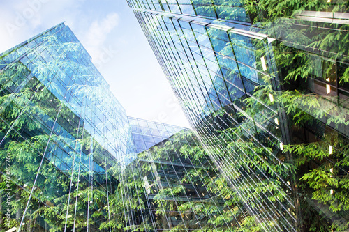 Slika na platnu green city - double exposure of lush green forest and modern skyscrapers windows