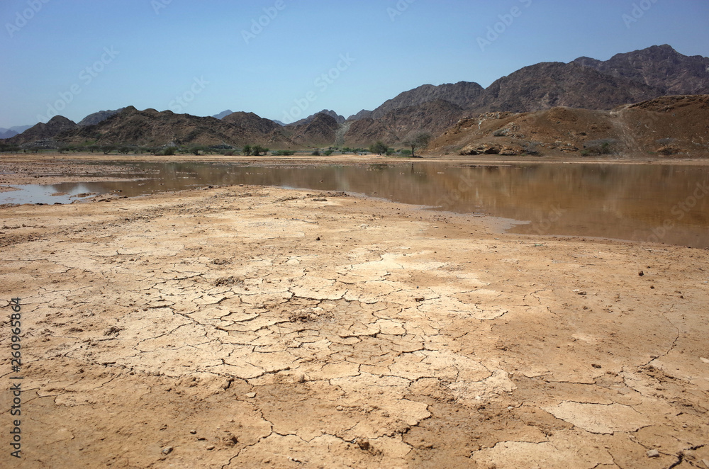 Desert landscape with cracked mud, puddle and dry mountains in Fujairah, United Arab Emirates