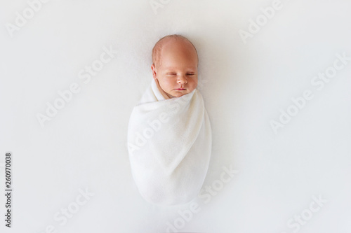 Newborn baby sleeps in white winding on a white background