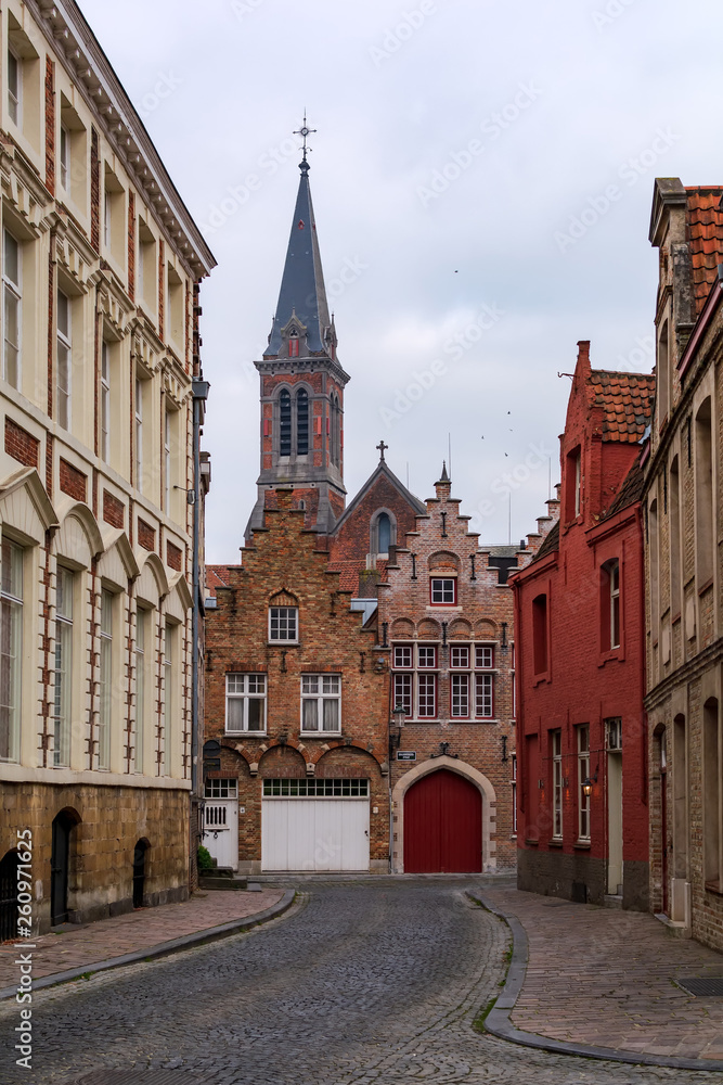 Old street of Bruges with traditional medieval houses of red brick with Heilig Hartkerk, former Jesuit church, tower in the background. Cityscape of Bruges streets.