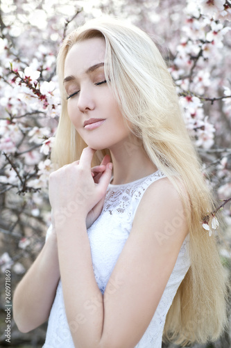 Young beautiful blonde woman in blooming almonds garden. 