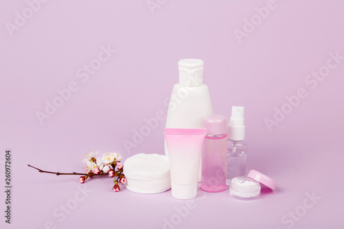Face and body care products with spring bloom (tonic or lotion, serum, cream, shampoo, micellar water, cotton pads and sticks, shaver) on purple. Freshness and body care. Skin cosmetics. Border banner