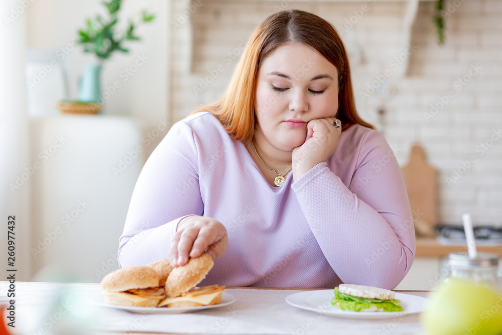 Cheerless plump woman thinking about the burger Cheerless plump woman thinking about the burger