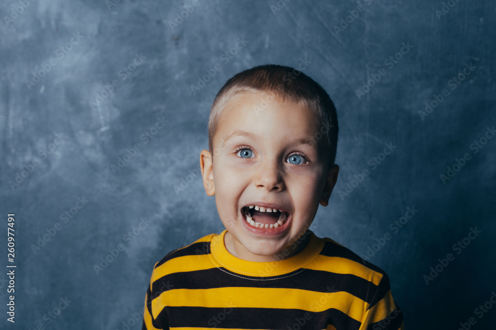 Portrait of a screaming child with open mouth, A little boy poses in front of a gray-blue concrete wall. Portrait of a screaming child with open mouth, A little boy poses in front of a gray-blue concrete wall.