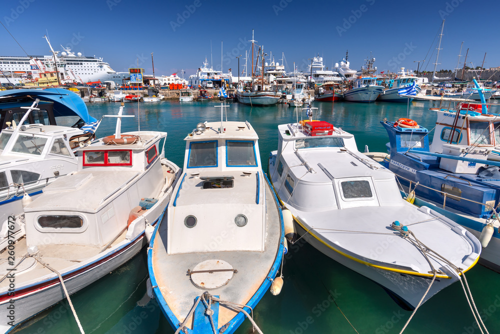 Rhodes, Greece - August 2016: Fishing boats, cruise ships for tourists and luxury floating hotels are anchored at docks in the new Mandraki harbor of the Old Medieval City of Rhodes in Dodecanese.
