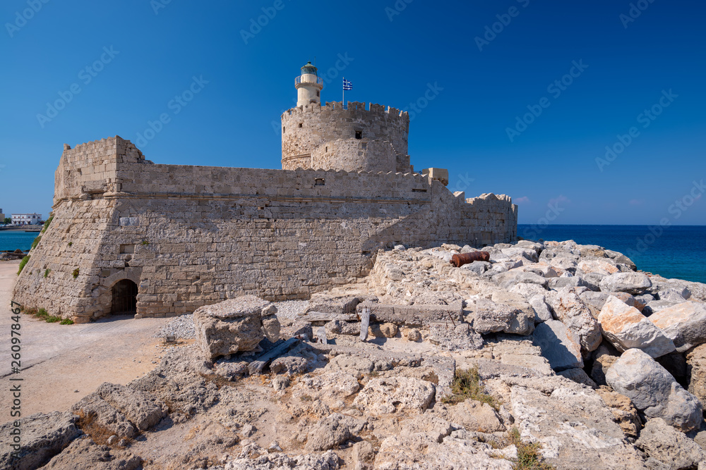 The medieval Fort of Saint Nicholas in the old Mandraki harbour of Rhodes, Dodecanese, Greece, is famous and popular tourist summer destination. Stone building on the seashore against clear blue sky.