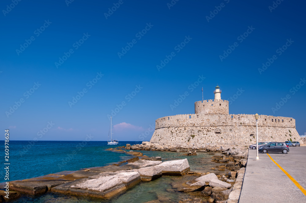The medieval Fort of Saint Nicholas in the old Mandraki harbour of Rhodes, Dodecanese, Greece, is famous and popular tourist summer destination. Stone building on the seashore against clear blue sky.