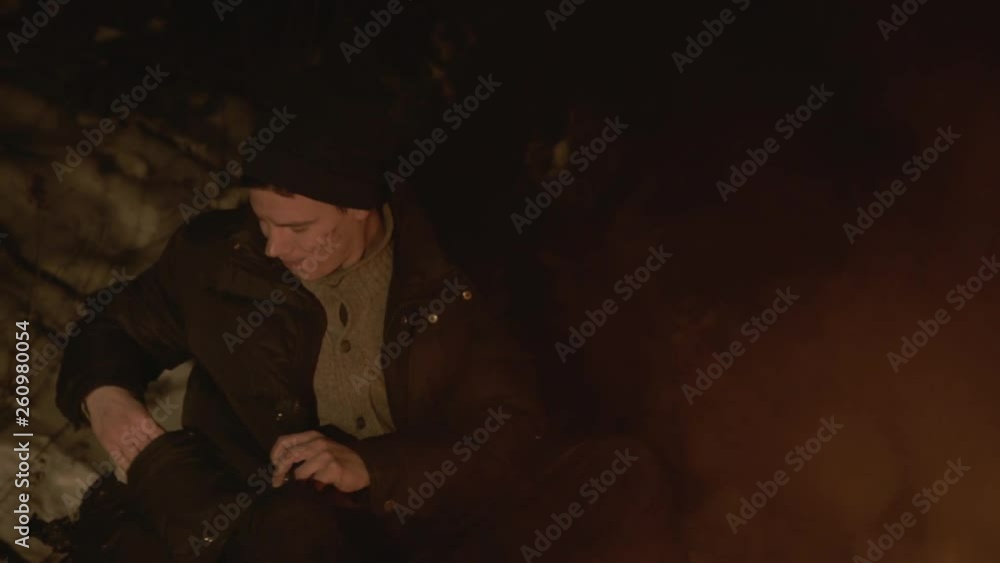 Homeless man gets and eats a roll at campfire in night Homeless man gets and eats a roll at campfire in night