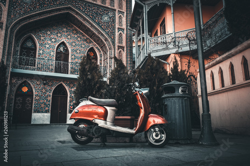 Old vintage orange Italian scooter parked on pavement in old city of Tbilisi, Georgia near Orbeliani mosque in Abanotubani district