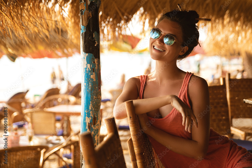Fototapeta Młoda kobieta jest ubranym okulary przeciwsłonecznych siedzi w plażowym barze