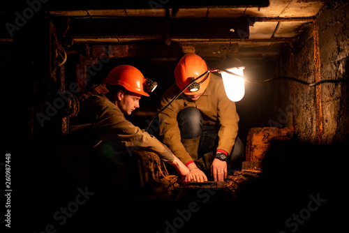 Two young guys in a working uniform and protective helmets, sitting in a low tunnel. Workers of the mine. Miners