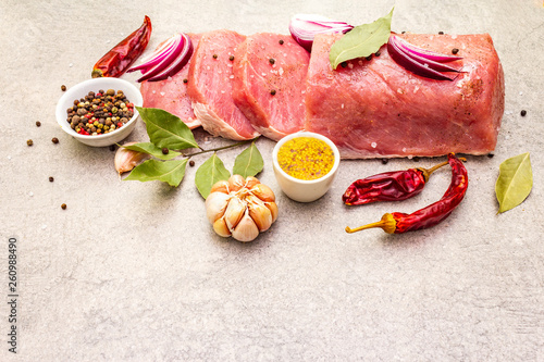 Raw pork tenderloin with vegetables and spices. Cooking meat background, fresh brisket boneless steak on stone background, copy space.