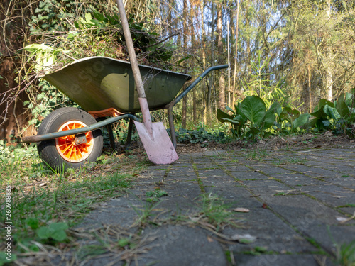 Wheelbarrow filled with leaves and branches with a fanned spade after gardening in spring