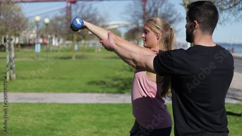 Concentrated woman training arms with dumbbells. Sporty young girl and man or instructor doing exercise. Concept of sport photo