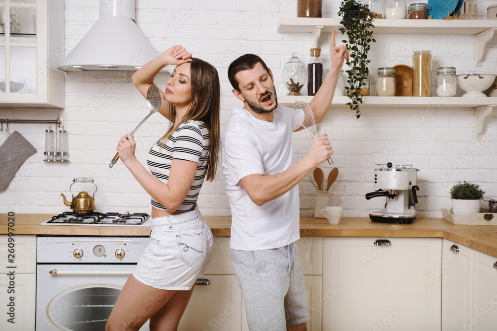 Funny young couple dancing and singing music together enjoying cooking in the kitchen, man and woman in love having fun preparing breakfast food feeling happy and carefree on weekend lifestyle at home Funny young couple dancing and singing music together enjoying cooking in the kitchen, man and woman in love having fun preparing breakfast food feeling happy and carefree on weekend lifestyle at home