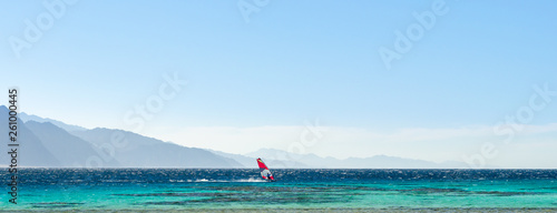 surfer rides in the Red Sea against the backdrop of high rocky mountains and a blue sky with clouds in Egypt Dahab