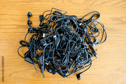 A lot of black music earphones pile together as a electronics waste on the wood background