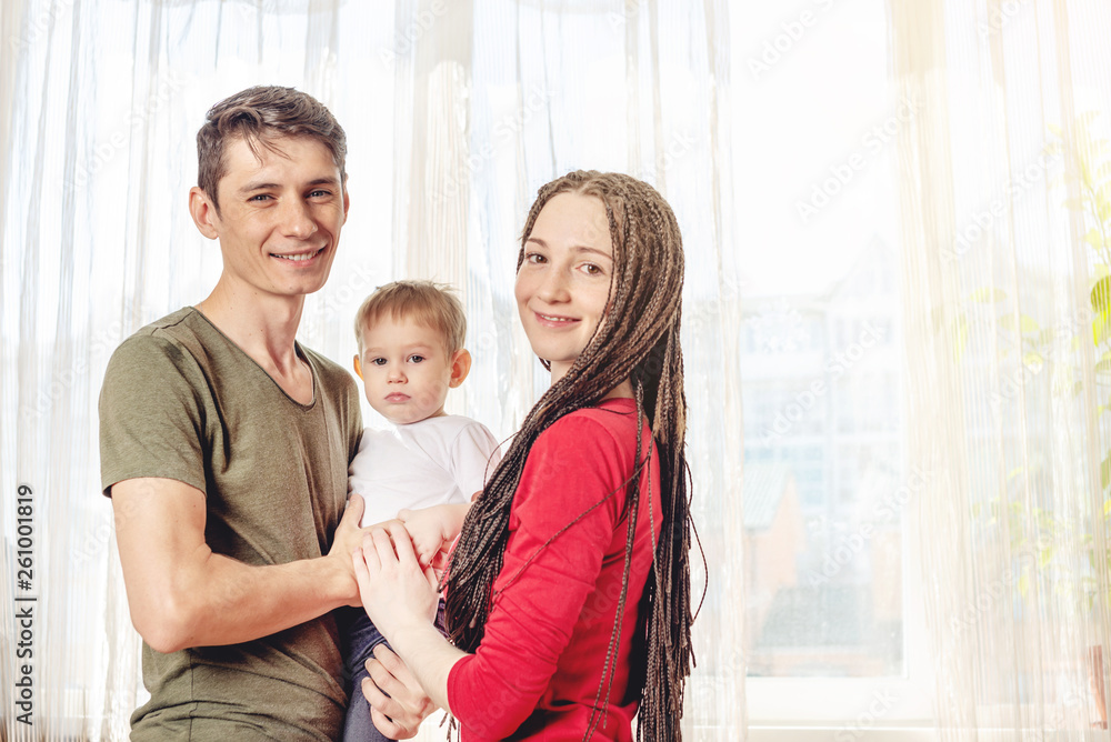 Happy parents father and mother playing with baby son at the in the morning on window background. Cheerful young family Happy parents father and mother playing with baby son at the in the morning on window background. Cheerful young family