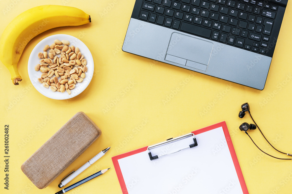 Yellow workplace with laptop, banana and peanuts. Snack at work. Top view. Flat lay Yellow workplace with laptop, banana and peanuts. Snack at work. Top view. Flat lay