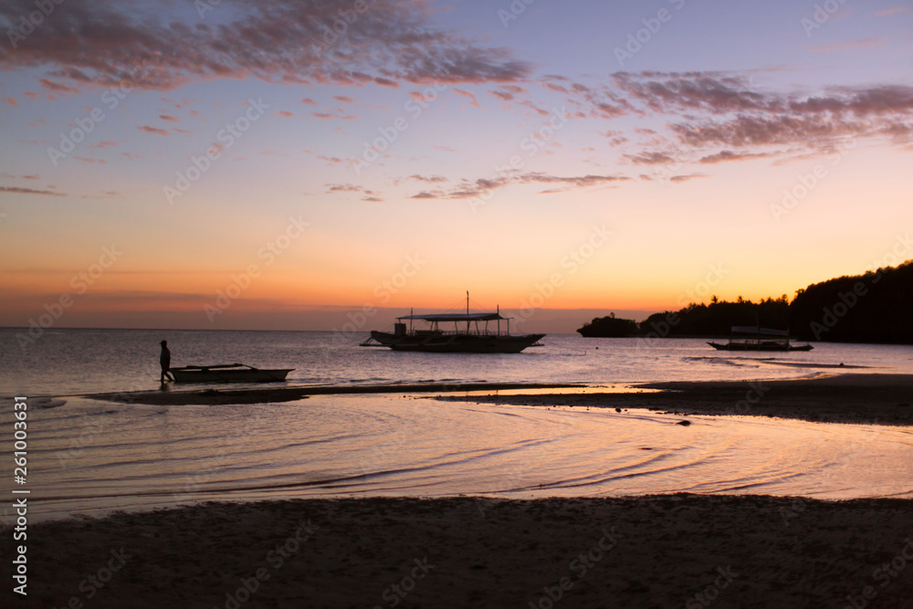 Naklejka premium outrigger dive and fishing boat at the beach on the white sand, in a tranquil summer sunset dusk background photo