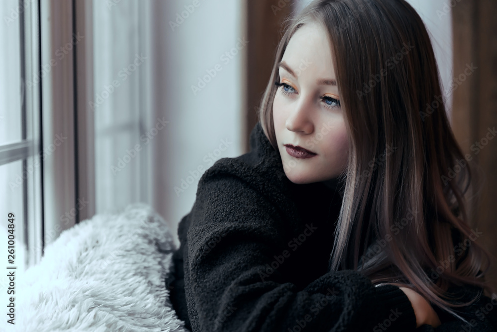 beautiful young girl sitting alone on the windowsill and looking out the window.