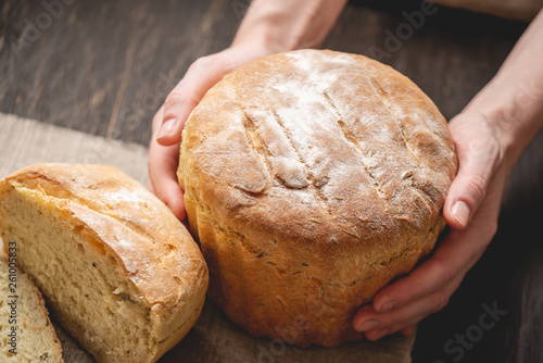 Female hands holding homemade natural fresh bread with a Golden crust on a napkin on an old wooden background