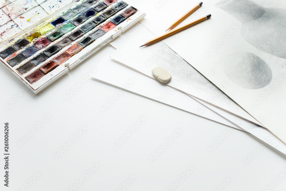 Watercolor paints, pencils, eraser, drawings on a white table. Place to copy space. Watercolor paints, pencils, eraser, drawings on a white table. Place to copy space.