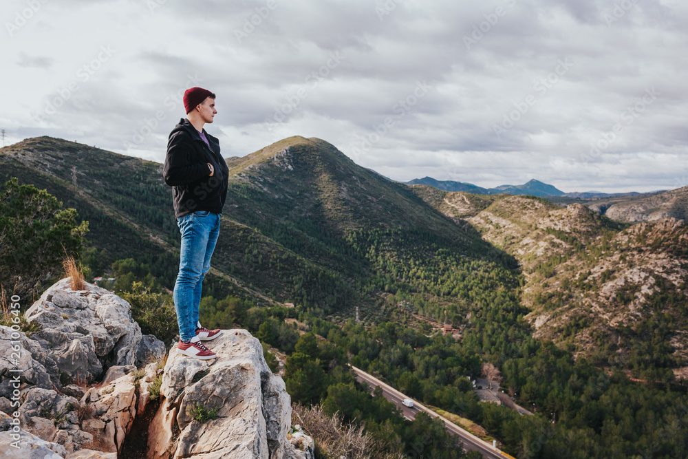 Fototapeta premium Young male enjoys mountains and nature. Nice landscape scenery. Highway with cars in background.