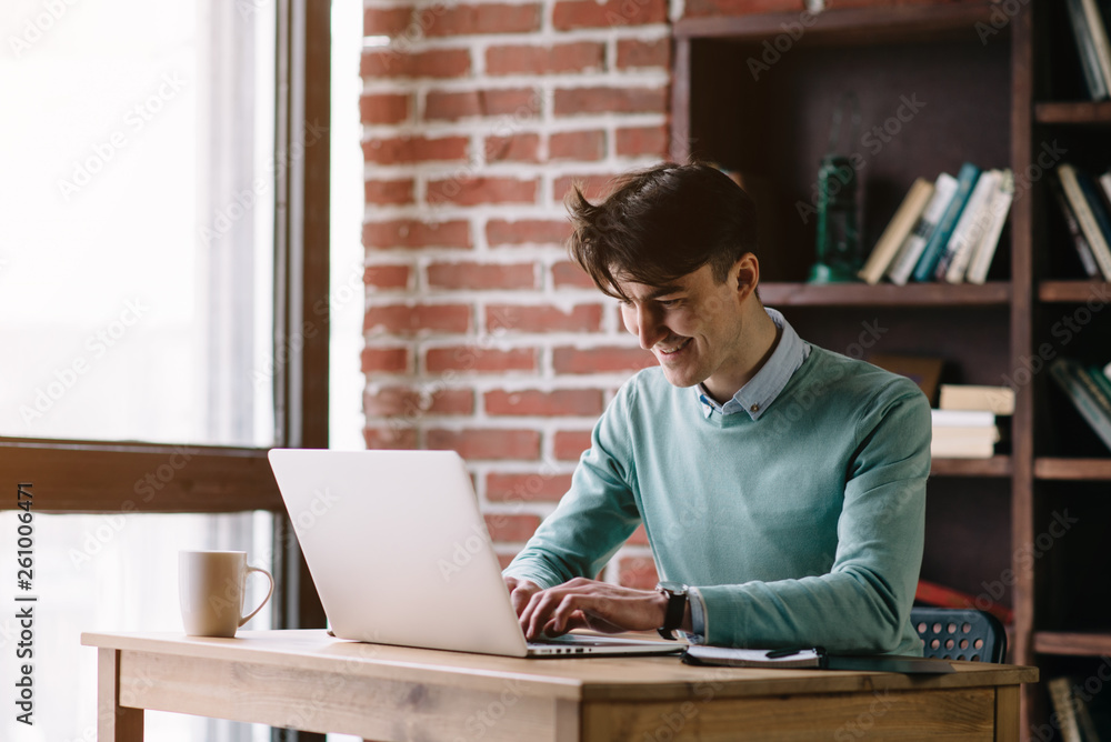 Fototapeta premium Young handsome student typing on his notebook his diploma. Student discussing on the phone universities's timetable. Education online. Work on freelance. Software development.