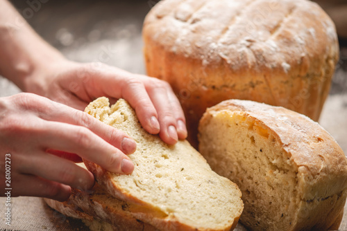 Women's hands breaking homemade natural fresh bread with a Golden crust on old wooden background. Baking bakery products