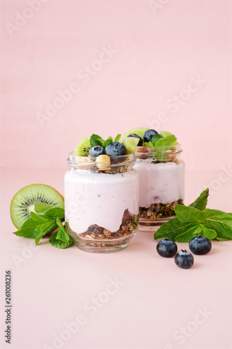 Blueberry Parfaits with homemade granola and kiwi in glass jar. Pastel pink background, close-up view